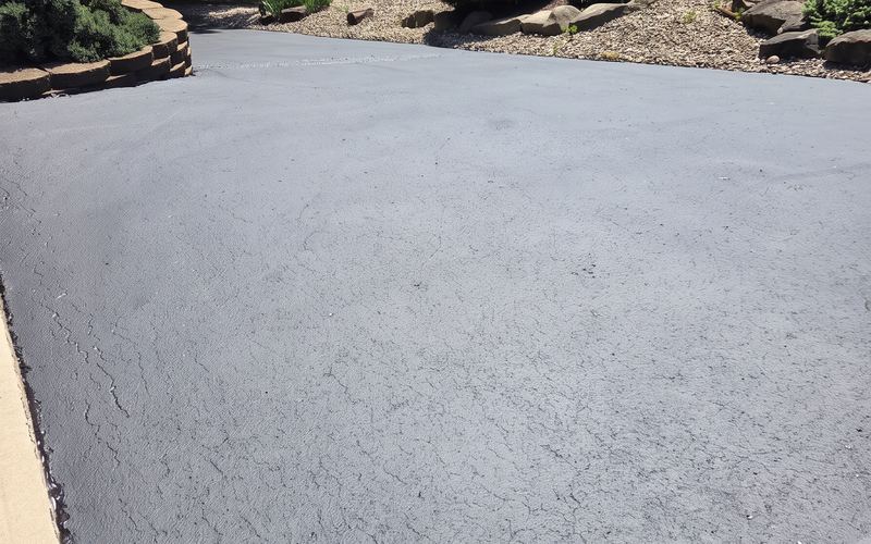 Finished black asphalt driveway in front of a brick home