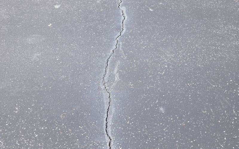 Cracked asphalt driveway edge beside grass