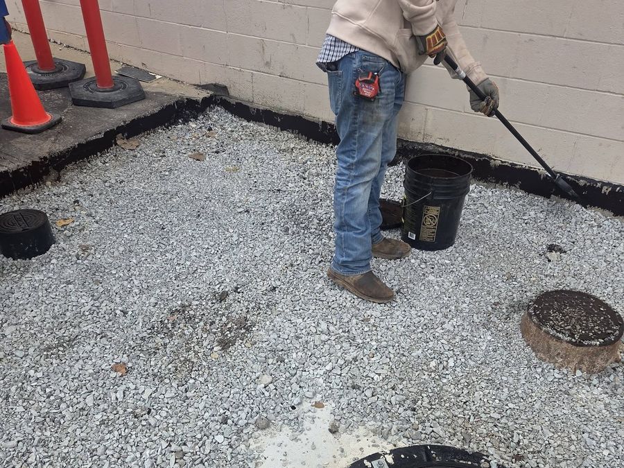 Crew member preparing a compacted stone base beside a block wall